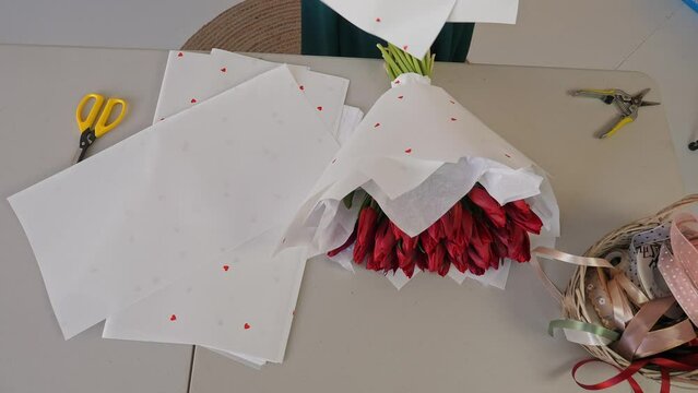 Caucasian lady florist gives a pen, the basis for a bouquet of tulips. A professional makes a fresh bouquet. Small business.