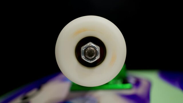 Rapidly spinning skateboard wheel steadily loses speed and comes to a stop. Close macro shot shows wheel nut and bearings, skate truck is visible in soft focus.