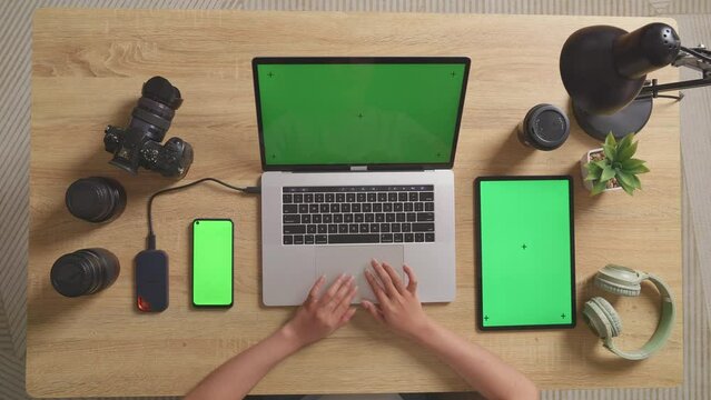 Top View Zoom Out Shot Of A Woman Video Editor Using Green Screen Laptop With Green Screen Smartphone And Tablet Next To The Camera In The Workspace At Home
