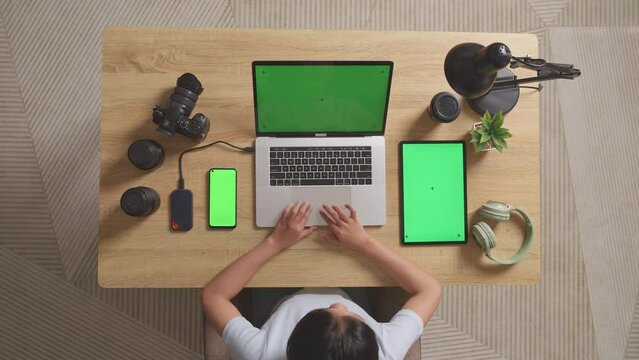 Top View Zoom In Shot Of A Woman Video Editor Using Green Screen Laptop With Green Screen Smartphone And Tablet Next To The Camera In The Workspace At Home
