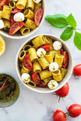 Rigatoni pasta with pesto, tomatoes and mozzarella in white bowl. Italian cuisine concept.
