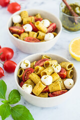 Rigatoni pasta with pesto, tomatoes and mozzarella in white bowl. Italian cuisine concept.