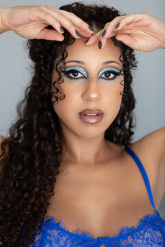 Boudoir portrait of a beautiful mixed race woman in her late 20s. She is wearing a blue bra and is wearing blue eyeshadow. She has curly brown hair and eyes. 