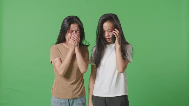 A Young Asian Woman Victim Of Violence With Bruise On Body Crying While Another Woman Talking On Smartphone Asks For A Help In Green Screen Background Studio
