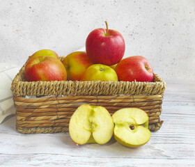 Wicker basket with red juicy apples close up on a wooden white table. Two halves of an apple. Collection of fruits. healthy food concept. place for text