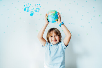 Smiling caucasian boy holding an earth globe model over his head on the background with stars and...
