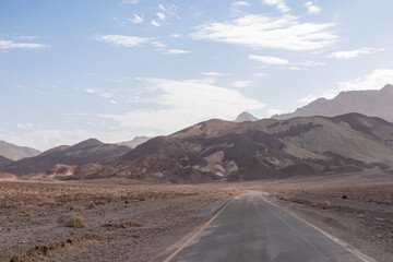 Panoramic view of endless empty road leading to colorful geology of multi hued Artist Palette rock formations in Death Valley National Park near Furnace Creek, California, USA. Black mountains