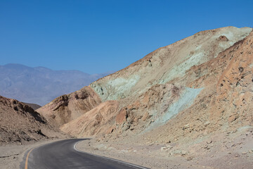 Panoramic view of endless empty road leading to colorful geology of multi hued Artist Palette rock formations in Death Valley National Park near Furnace Creek, California, USA. Black mountains
