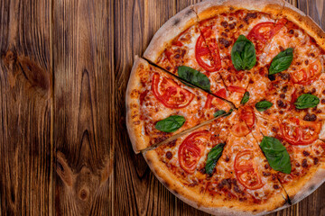 Delicious fragrant pizza-Margherita with mozzarella, tomatoes and basil on tomato sauce on woden background. Copy space