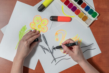 Women's manicured hands draw with felt-tip pens on a white sheet. At the desk. Top view