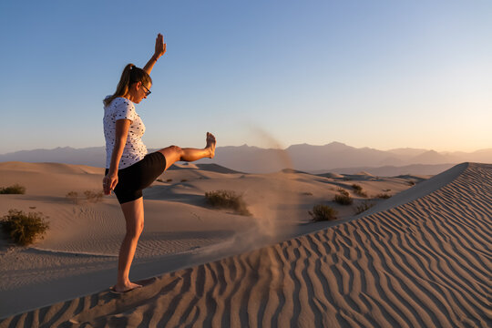 Woman having fun in the sand at sunrise with scenic view on Mesquite Flat Sand Dunes, Death Valley National Park, California, USA. Morning walk in Mojave desert with Amargosa Mountain Range in back