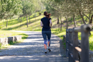 Fototapeta premium Sportive woman jogging in the green park - back view