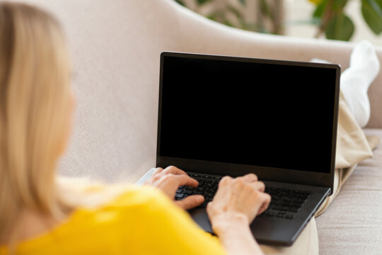 Millennial caucasian blonde lady in yellow clothes typing on computer with blank screen