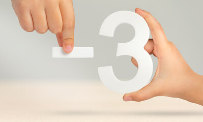 Minus three. The number three and the minus symbol in a hand close-up on a light gray background....