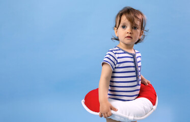 Fototapeta na wymiar Studio photo of Young child with lifebelt at blue background. Summer sea travel concept. 