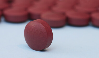 One red-brown medical pill close-up on a blue background and on the background of a pile of pills.
