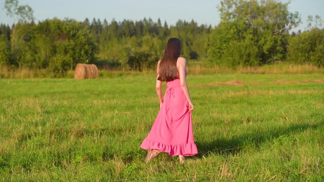 woman walks across the field in a pink dress
