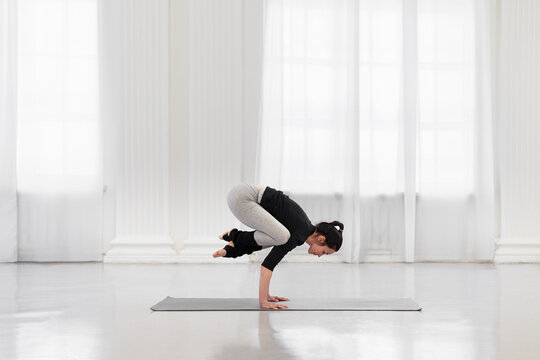 Side view of charming woman doing bakasana during yoga meditation in a bright gym. The concept of arm strength and endurance, flexibility and balance