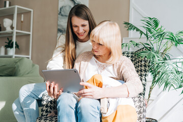 Senior woman and daughter playing with tablet pc. Smiling older woman and her granddaughter sitting home using gadget digital device for online shopping internet surfing video conference calling.