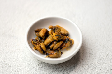 Fried mussels in white plate. Seafood. Cooked mussels. Salad ingredient. White background. Close-up. Soft focus. Copy space.