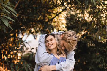 Portrait of beautiful blonde curly girl looking away with happy smile while man kissing her neck. Happy couple walk in park.