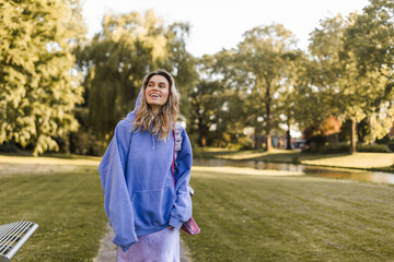 Portrait of beautiful confident woman laughing in nature, walk in park and look by side. Blonde curly woman look by side, enjoy of nature, amazement woman in purple hoody.