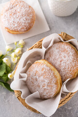 Ruddy donuts berliners with filling sprinkled with powdered sugar in basket on a grey background