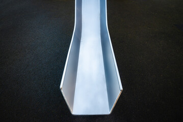 Closeup, bottom of steep stainless steel silver chrome slide. Children's playground. Dark background