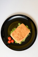 Cooked panini with green lettuce on a black plate with cherry tomatoes.