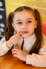 A small and beautiful girl is eating french fries in a cafe.