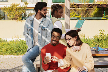 Glad millennial multiethnic modern students look at smartphone, have video call, study together