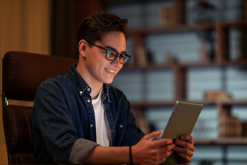 Happy young guy businessman using digital tablet at dark office
