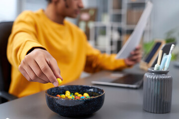 Close up of young man eating snacks while working or studying at home, focus on hand holding...