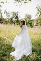 Happy bride holding her pale pink dress. A long veil that beautifully follows the bride. The look of the girl from behind the shoulder. Morning of the bride in the garden. Spring wedding