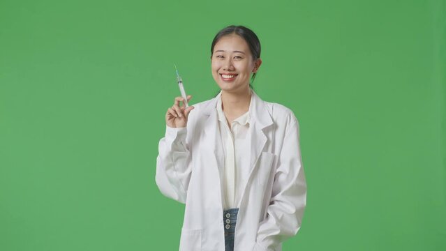 Asian Woman Doctor Holding A Syringe And Smiling On Green Screen Background In The Hospital
