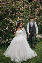 Fototapeta premium Happy stylish groom walking to the bride. The bride is in the foreground. Groom in a vest. Portrait of the groom. Spring wedding