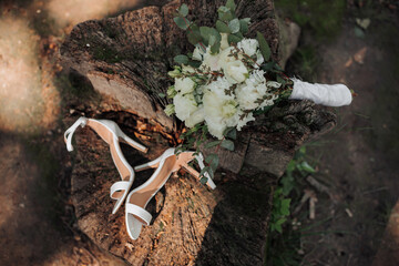 wedding bouquet on a tree. Wedding details on a wooden stump in the park. A beautiful bouquet of white flowers. Bride's shoes
