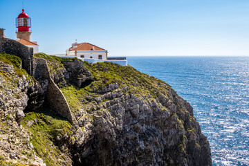 The lighthouse Farol do Cabo de São Vicente atop the breathtaking high rugged cliff of Cabo de São Vicente headland, the southwesternmost point of Europe, over the Atlantic Ocean on a sunny May day.