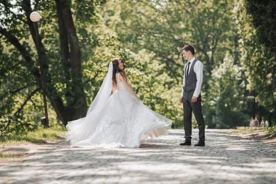 Groom and bride in the garden. Spring wedding in the park. Happy wedding couple running in the park. The bride is circling with her dress. Stylish and beautiful. Photo from the back. Princess dress.