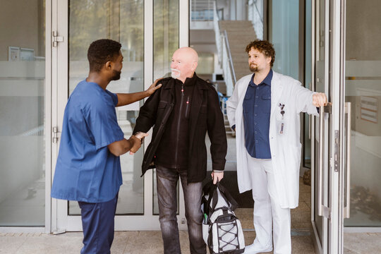 Senior male patient shaking hands with nurse while standing by doctor at hospital doorway