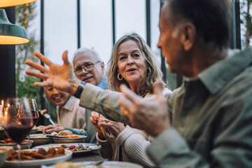 Senior woman listening to male friend gesturing while talking at dinner party