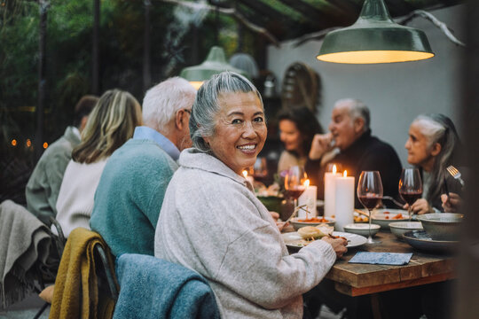 Smiling senior woman looking over shoulder while sitting with friends at dinner party