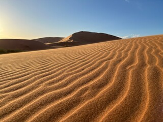 Dunes in the Sahara desert, Merzouga desert, grains of sand forming small waves on the dunes, panoramic view. Setting sun. Morocco
