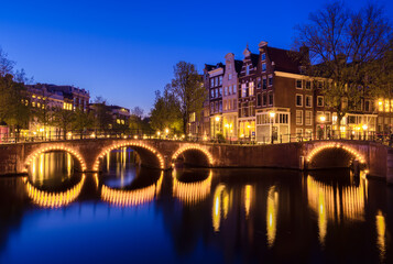 Fototapeta na wymiar A tranquil evening in Amsterdam, illuminated by the soft glow of dusk. A beautiful arch bridge reflects on a canal amidst stunning architecture and river views.