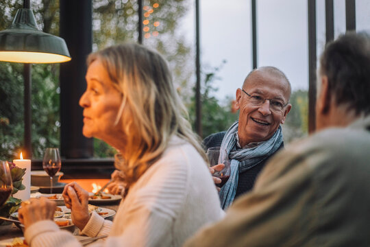 Smiling retired man talking to male friend at dinner party