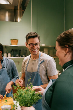 Happy male student talking to female friend during cooking class in kitchen