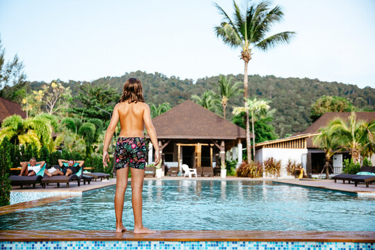 Rear view of shirtless girl standing at poolside in tourist resort during vacation