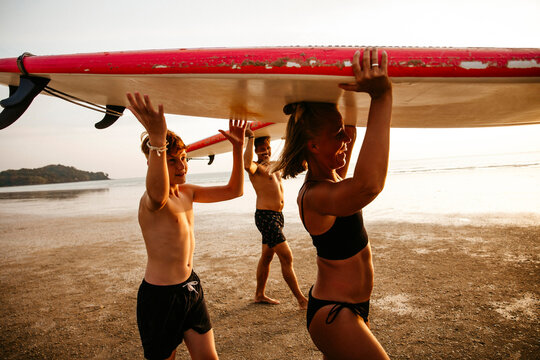 Happy family carrying paddleboards on heads while walking at beach during sunset
