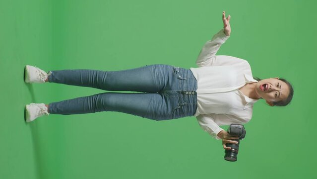 Full Body Of Puzzled Asian Photographer Using A Camera Taking Pictures, Saying Why And Making Gestures Doubtfully While Standing On Green Screen Background In The Studio
