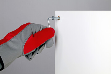 A man in a red protective glove is screwing a confirmat screw into a white furniture board with copy space